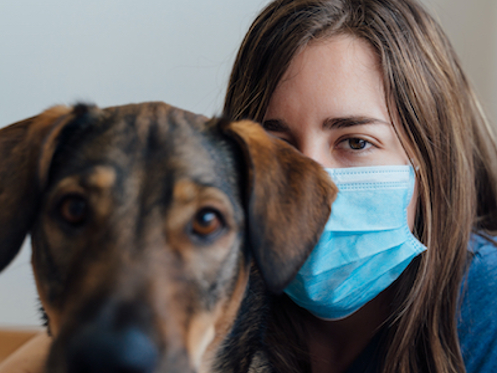 Woman wearing a surgical face mask, sitting with her dog